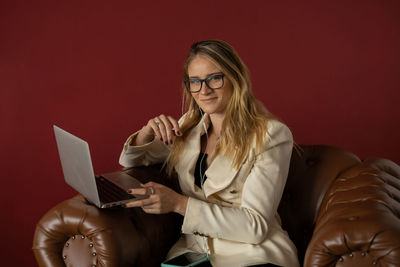 Woman working at home with laptop classic brown arm chair. red  wall home office. gray notebook 