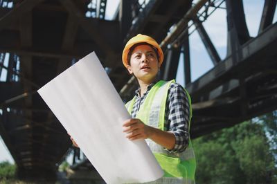 Engineer woman in hard hat holding walkie talkie while standing at construction site.