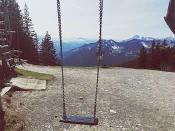 Empty swing hanging on mountain against sky
