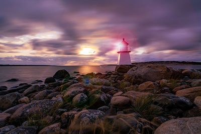 Lighthouse by sea against sky during sunset