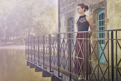 Young woman standing by railing against trees
