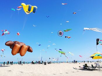 People flying kites at beach against clear blue sky