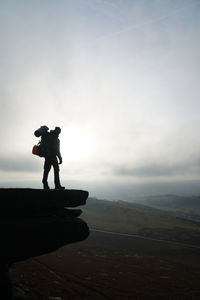 Silhouette man standing on edge of mountain against sky