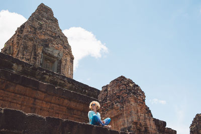 Low angle view of woman sitting on historic building against sky