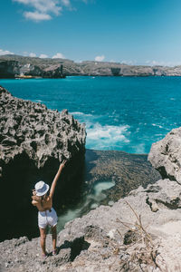 Rear view of woman standing on rock by sea