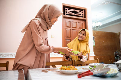 Mother passing plate to daughter at home