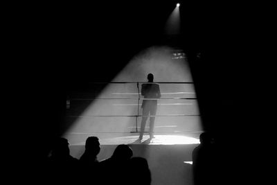 Rear view silhouette of man standing in boxing ring under spotlight