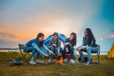 People relaxing on land against sky during sunset