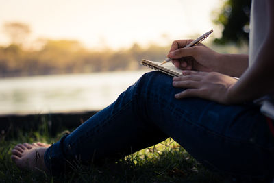 Low section of woman writing in book while sitting at park