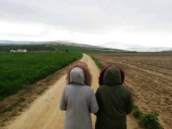 Rear view of women walking on dirt road against sky