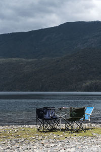 Chairs and table by lake against sky