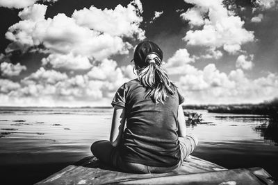 Rear view of woman sitting by lake against sky