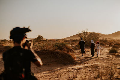 Rear view of people walking on field against clear sky