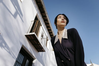 Beautiful woman looking away while standing by building during sunny day
