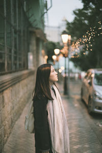 Thoughtful young woman looking away while standing on footpath in city