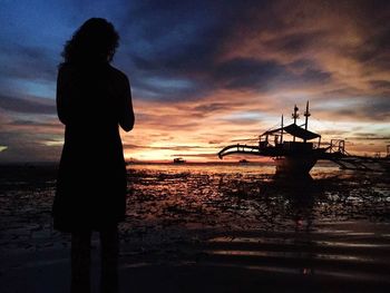 Silhouette man standing on beach against sky during sunset