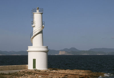 Lighthouse by sea against clear sky