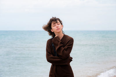 Young woman standing at beach against sky