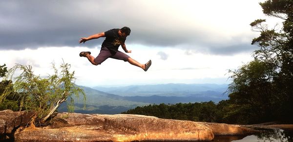 Man jumping over mountain against sky