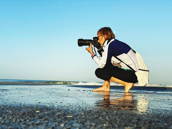 Man photographing in sea against clear sky