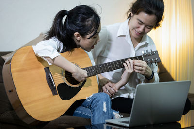 Mother teaching guitar to daughter at home
