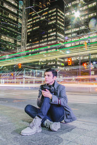 Portrait of woman sitting in illuminated city at night