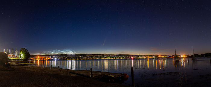 Illuminated city by sea against sky at night