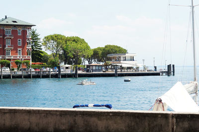 Sailboats moored on sea by buildings against sky