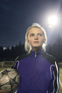 Girl holding soccer ball against sky at night