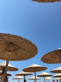 Low angle view of parasols against clear blue sky