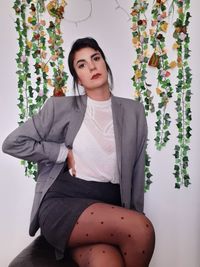 Portrait of beautiful young woman sitting against wall