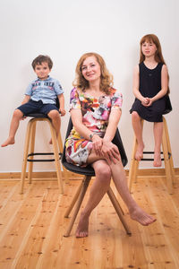 Portrait of smiling family sitting on chairs against wall