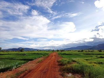 Empty road amidst agricultural field against sky