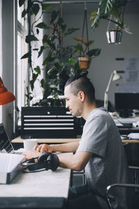 Side view of confident male hipster using laptop at desk in creative office