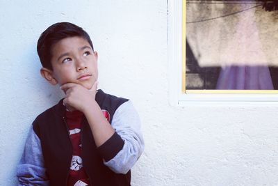 Thoughtful boy standing against white wall