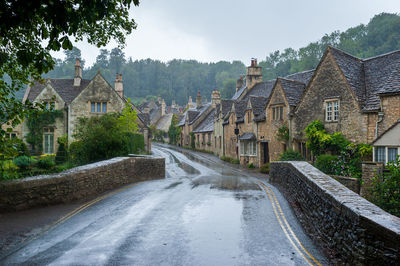 Houses by road amidst trees and buildings against sky