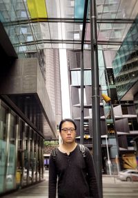 Portrait of young asian man standing in city street against buildings.