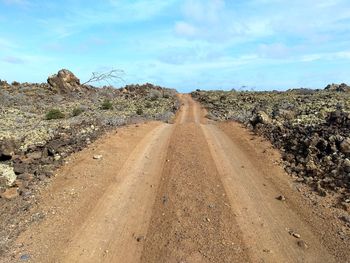 Dirt road amidst land against sky