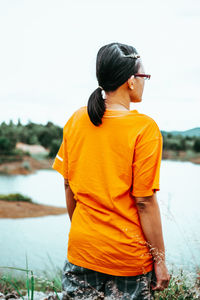 Rear view of young woman standing by lake against sky