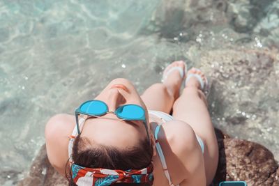 High angle view of woman wearing sunglasses sitting in sea during sunny day