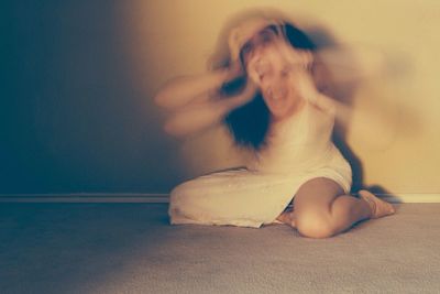 Blurred motion of woman screaming with holding head against wall