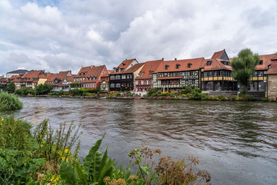 View of buildings by river against cloudy sky