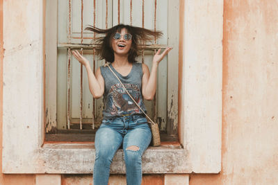 Happy young woman tossing hair while sitting on window sill