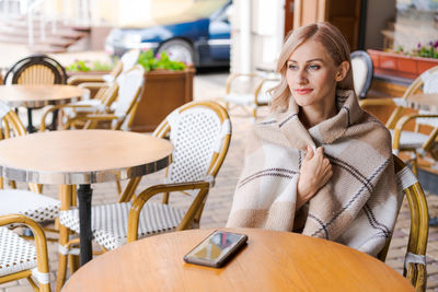 Young beautiful woman, in cafe, drinking coffee in cup, in cozy plaid happy