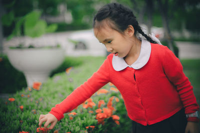 Girl plucking red flower from plant on field
