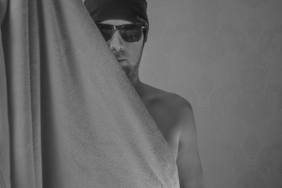 Portrait of young man wearing sunglasses standing against wall