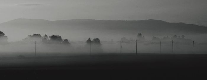 Electricity pylon on field against sky during foggy weather