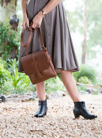 Low section of woman holding purse while standing on field at park