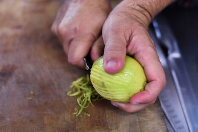 Cropped hand of man peeling lemon on cutting board