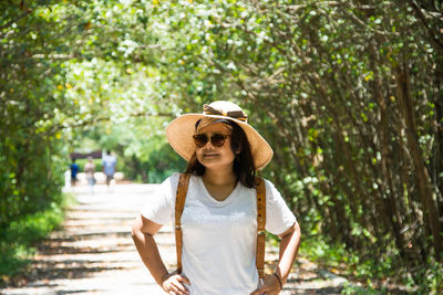 Smiling woman in sunglasses and sun hat on footpath during sunny day